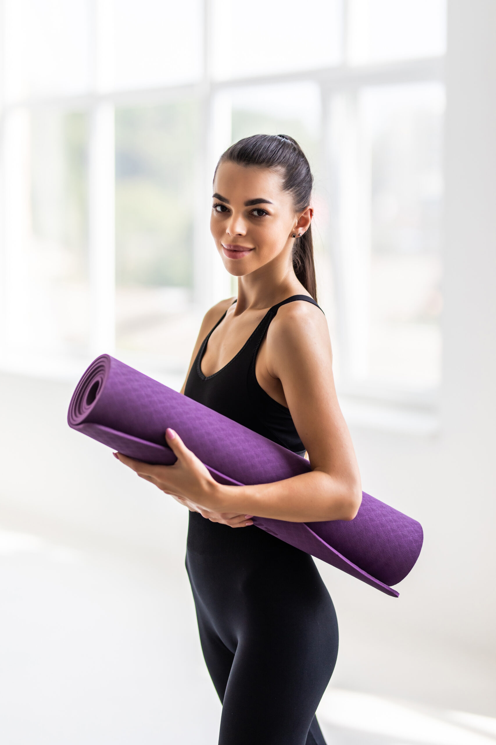 Beautiful young woman with a yoga mat at the gym